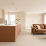 Cuisine moderne aux tons beiges avec îlot central terracotta et canapé marron assorti dans un salon lumineux.