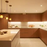 Cuisine moderne avec îlot central, éclairage suspendu et spots encastrés dans un ton chaud.