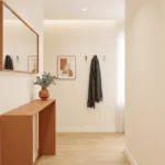 Une entrée lumineuse avec une console terracotta, un miroir mural, un cadre abstrait et des patères pour vêtements.