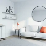Petit salon moderne aux tons neutres avec canapé gris, touches orange, miroir rond et console fine.
