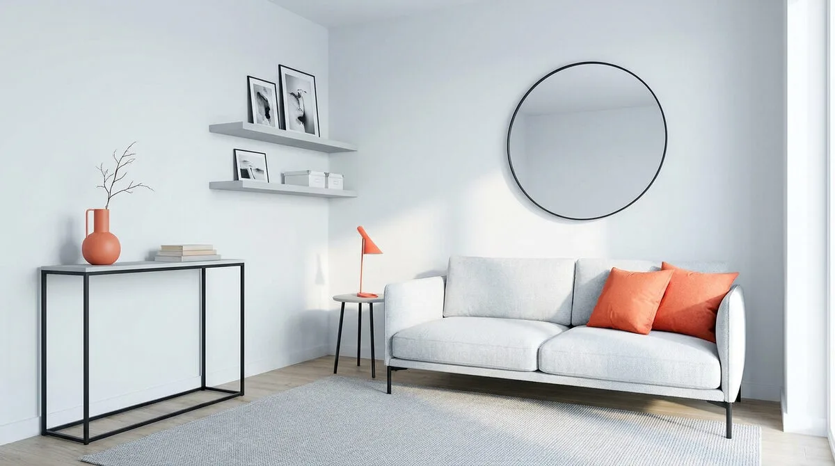Petit salon moderne aux tons neutres avec canapé gris, touches orange, miroir rond et console fine.