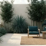Terrasse moderne avec bambous, plantes en touffe, fauteuils bleu canard et tapis en fibre naturelle.